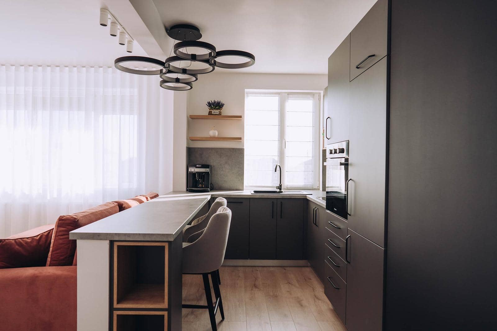 Apartament cu bucătărie grafit deschisă spre living, bar de mic dejun și canapea teracotă