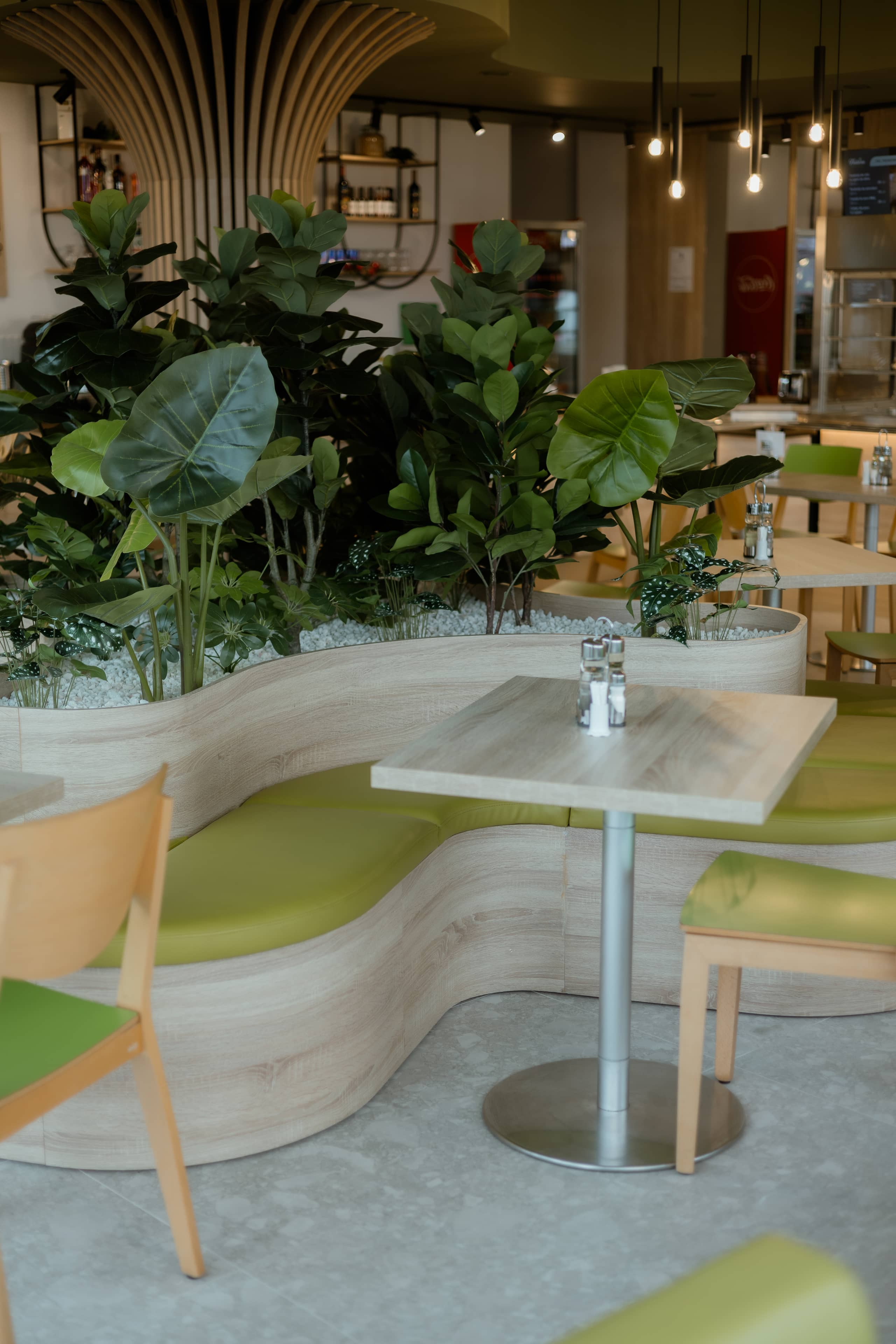 Banchetă curbă cu tapițerie verde, separată de circulație printr-o jardinieră de lemn