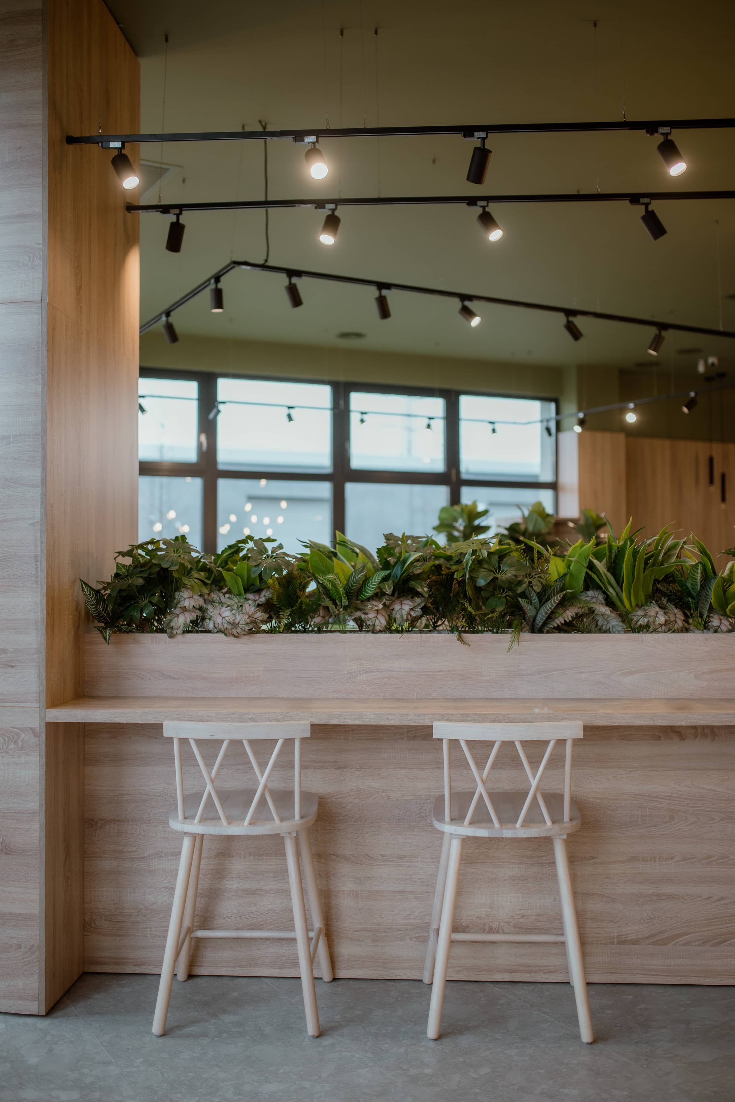 Bar înalt la fereastră, cu scaune albe și jardinieră continuă cu plante