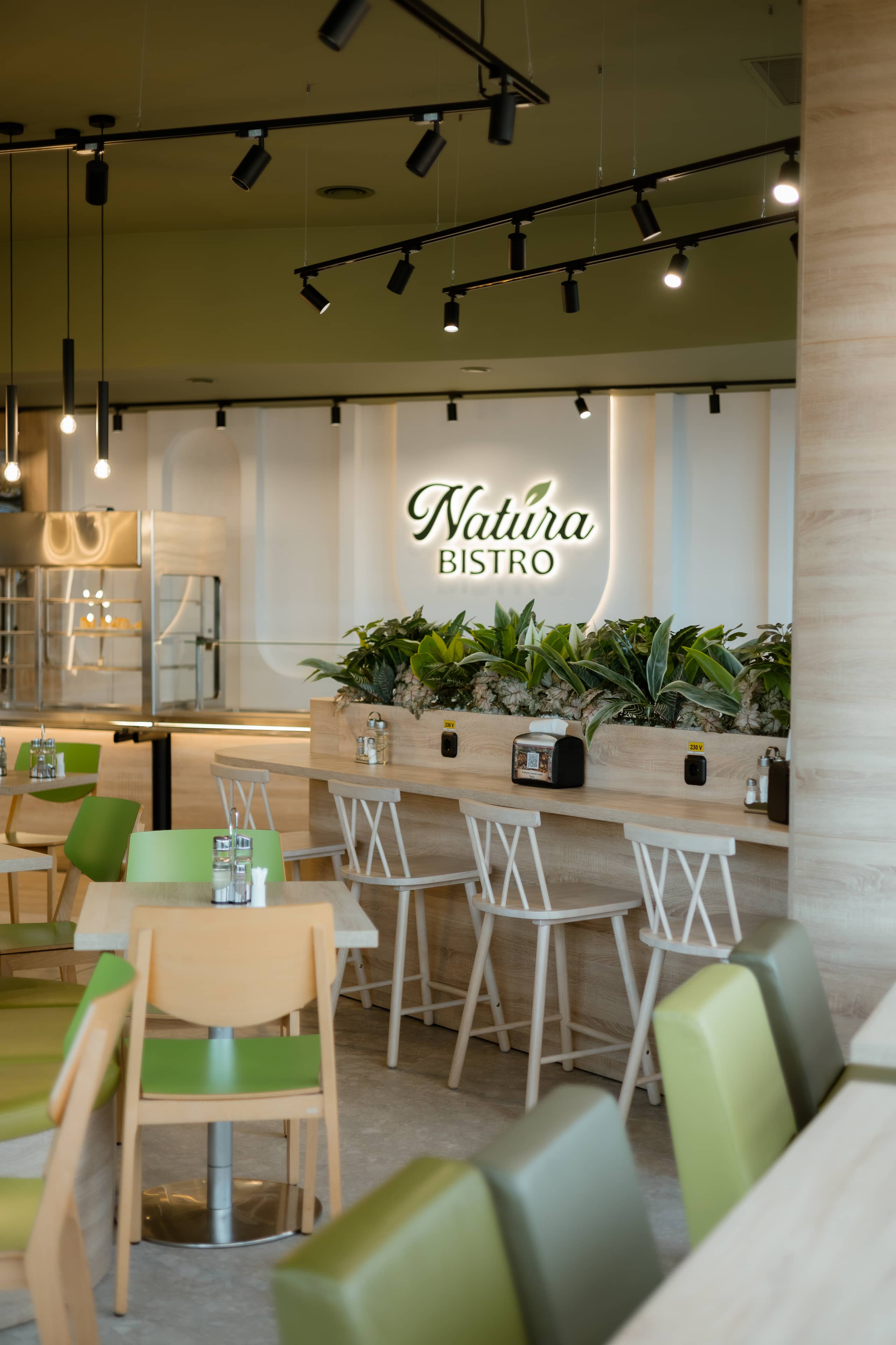 Zona de bar a bistroului, cu scaune înalte albe și logo luminos pe perete